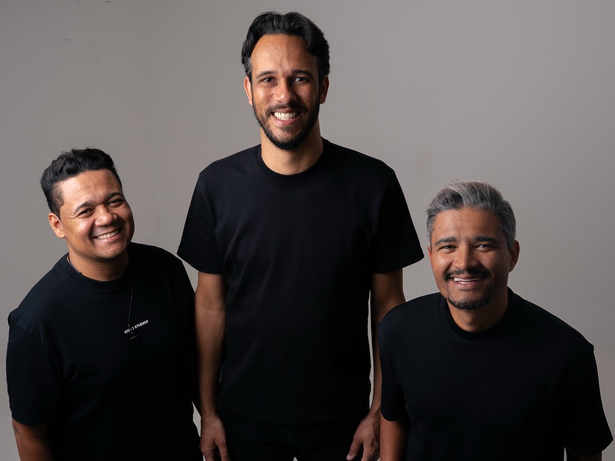 Os três integrantes do Omega Music, de camiseta preta, sorrindo em estúdio